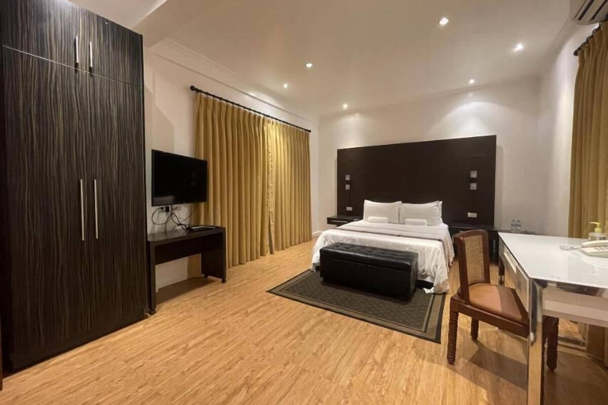 Ein modernes Hotelzimmer mit großem Kleiderschrank, einem Bett mit weißer Bettwäsche, einem Schreibtisch mit Stuhl und einem Fernseher.