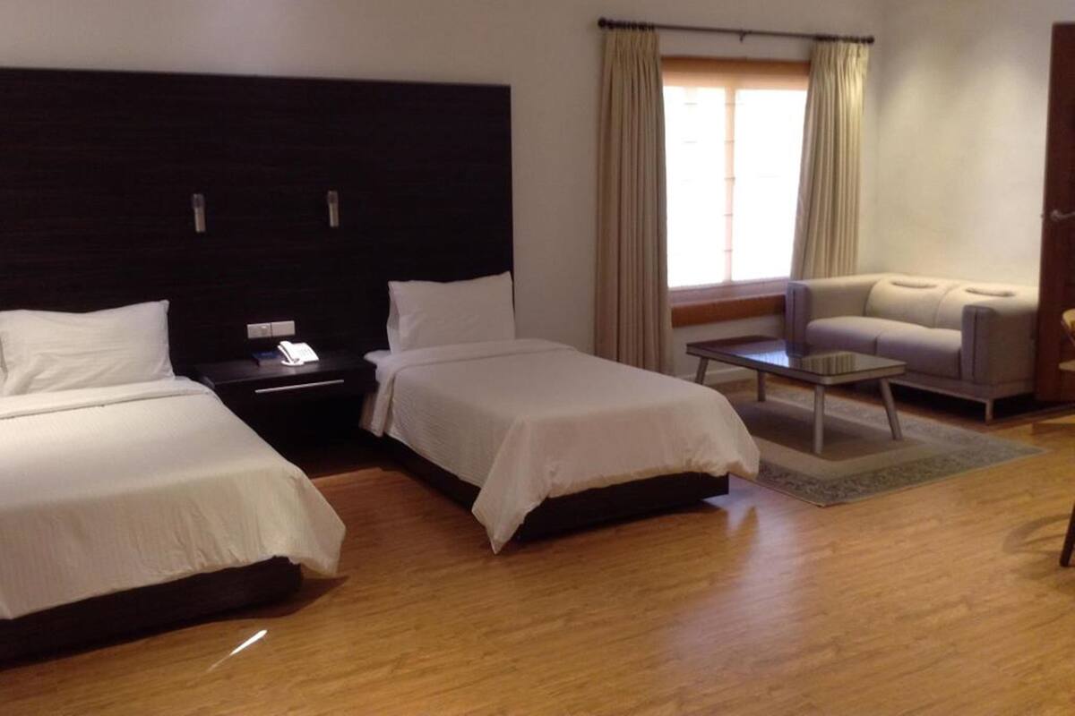 Ein Hotelzimmer mit zwei Betten, einem Schlafsofa, einem kleinen Tisch und einem Fenster mit Vorhängen.