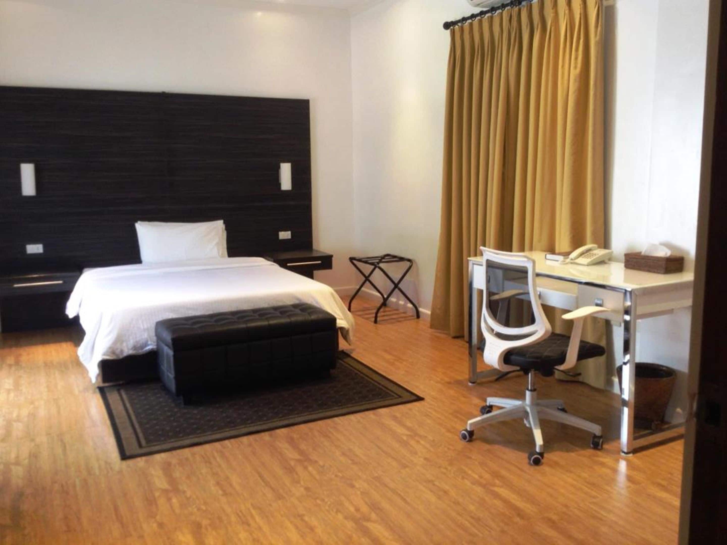 A hotel room with a bed, a desk with a chair, a telephone, and a trash bin.