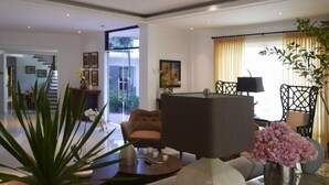 A modern living room with a sofa, a coffee table, and a lamp. There is a staircase leading to another room, and a window with curtains. - Bellagio Hills Hotel and Restaurant (Paoay)