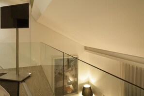 A modern interior with a glass railing, a flat-screen TV mounted on a stand, and a wall-mounted lamp.