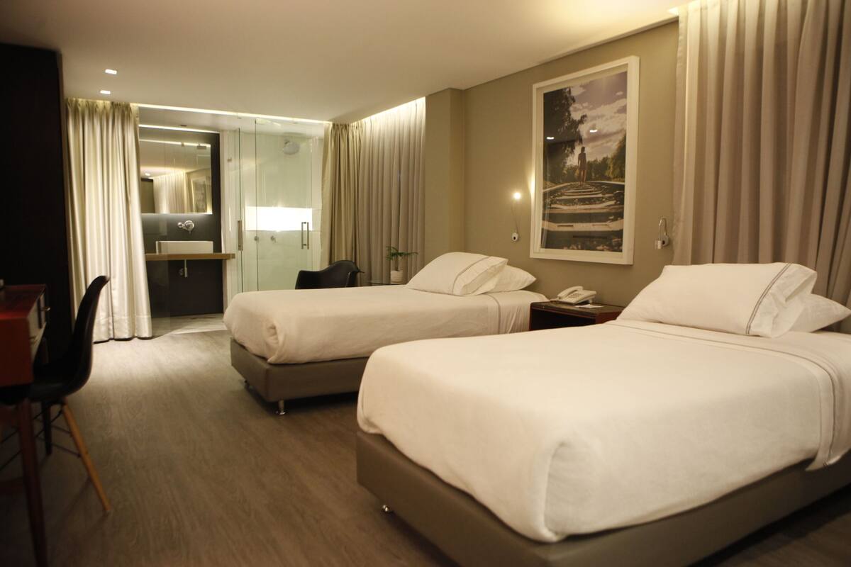 A hotel room with two beds, a desk, a chair, a nightstand, a mirror, and a painting on the wall.