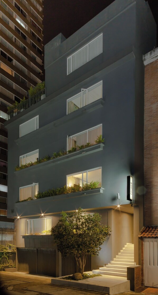 A multi-story building with balconies, a staircase, and a tree in the foreground.