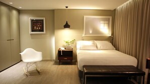 A hotel room with a bed, a chair, a bedside table with a lamp, a window with curtains, and a wall-mounted picture. - The Grace Hotel (Bogotá)