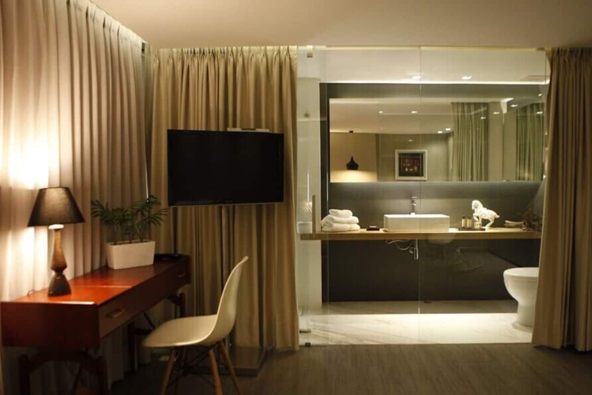A hotel room with a desk, chair, TV, and a bathroom with a sink and toilet.