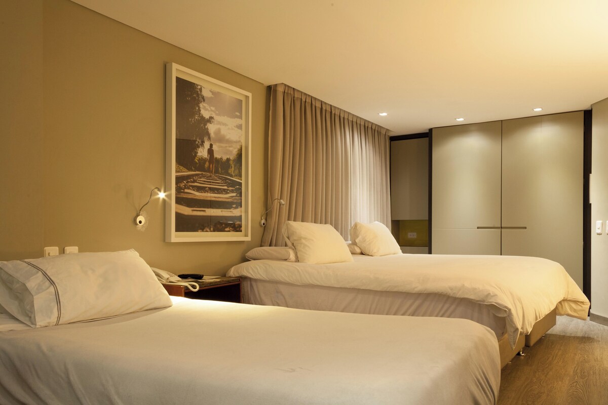 A hotel room with two beds, a painting on the wall, a nightstand with a phone, and a wardrobe.