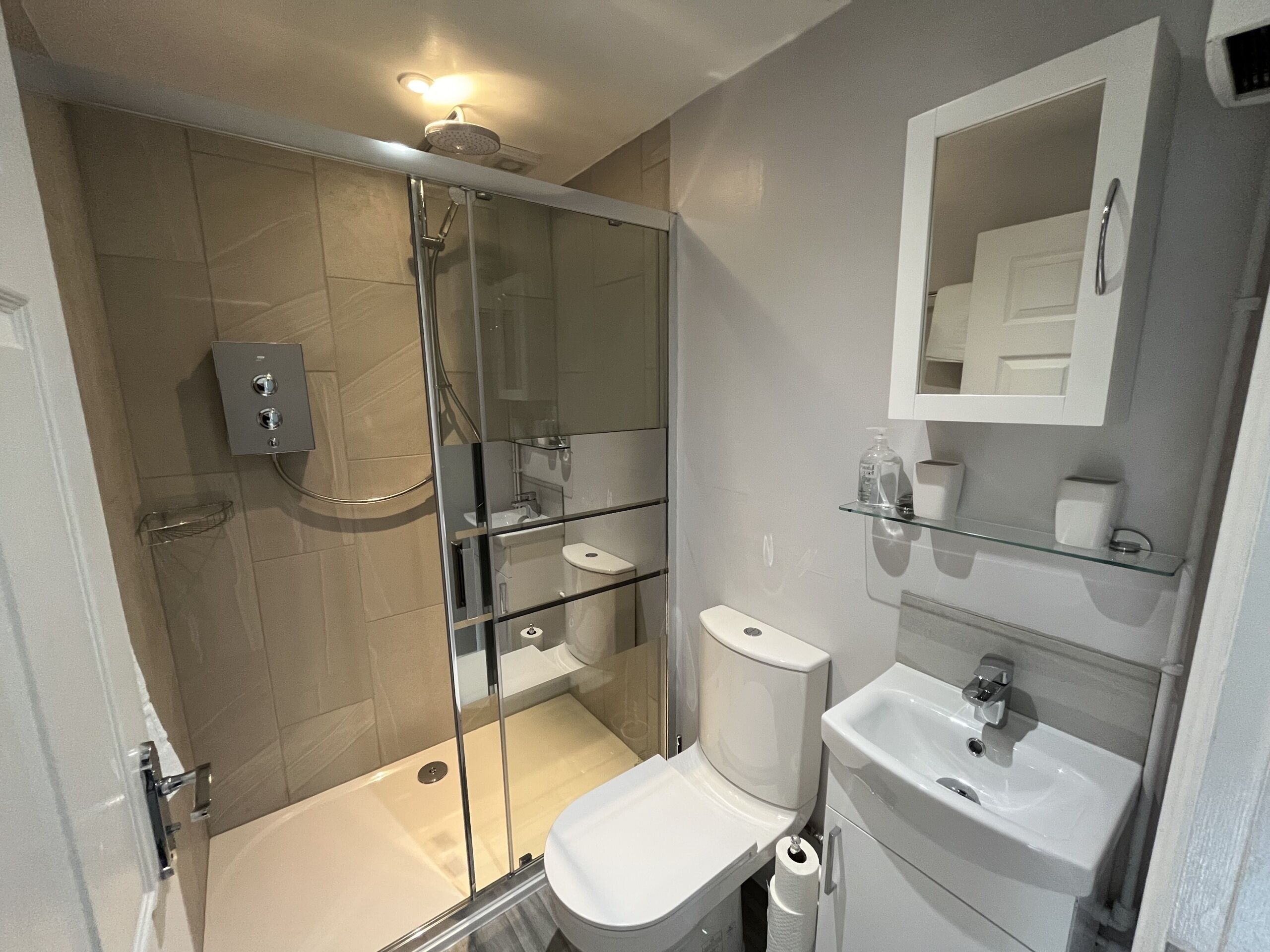 Een moderne badkamer met een douche met glazen wand, toilet en wastafel.