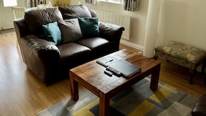 A living room with a leather sofa, a wooden coffee table, a small bench, and a radiator. - Cherry Tree Cottage (Chipping Norton)