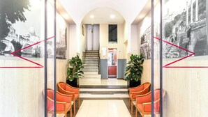 A reception area with a staircase, potted plants, and red chairs. - La dolce vita QG (Rome)