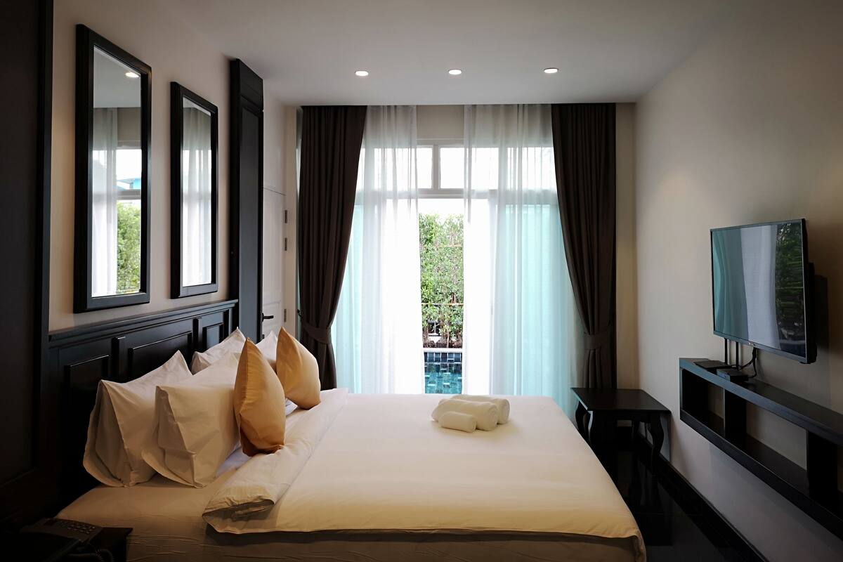 Une chambre d’hôtel avec un grand lit, une télévision, un bureau et une vue sur la verdure environnante.