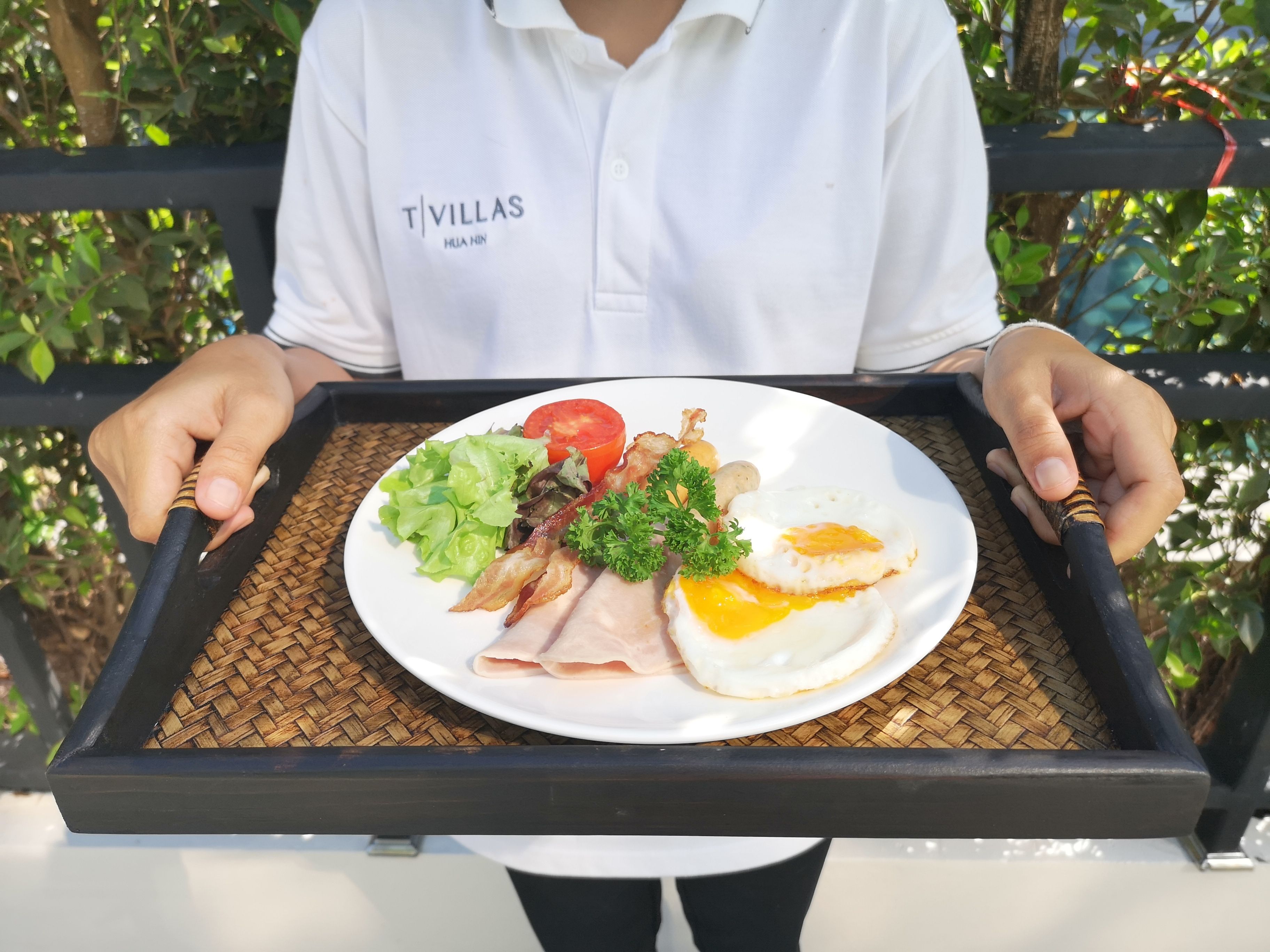 A person holding a tray with a plate of food including eggs, bacon, lettuce, tomato, and parsley.