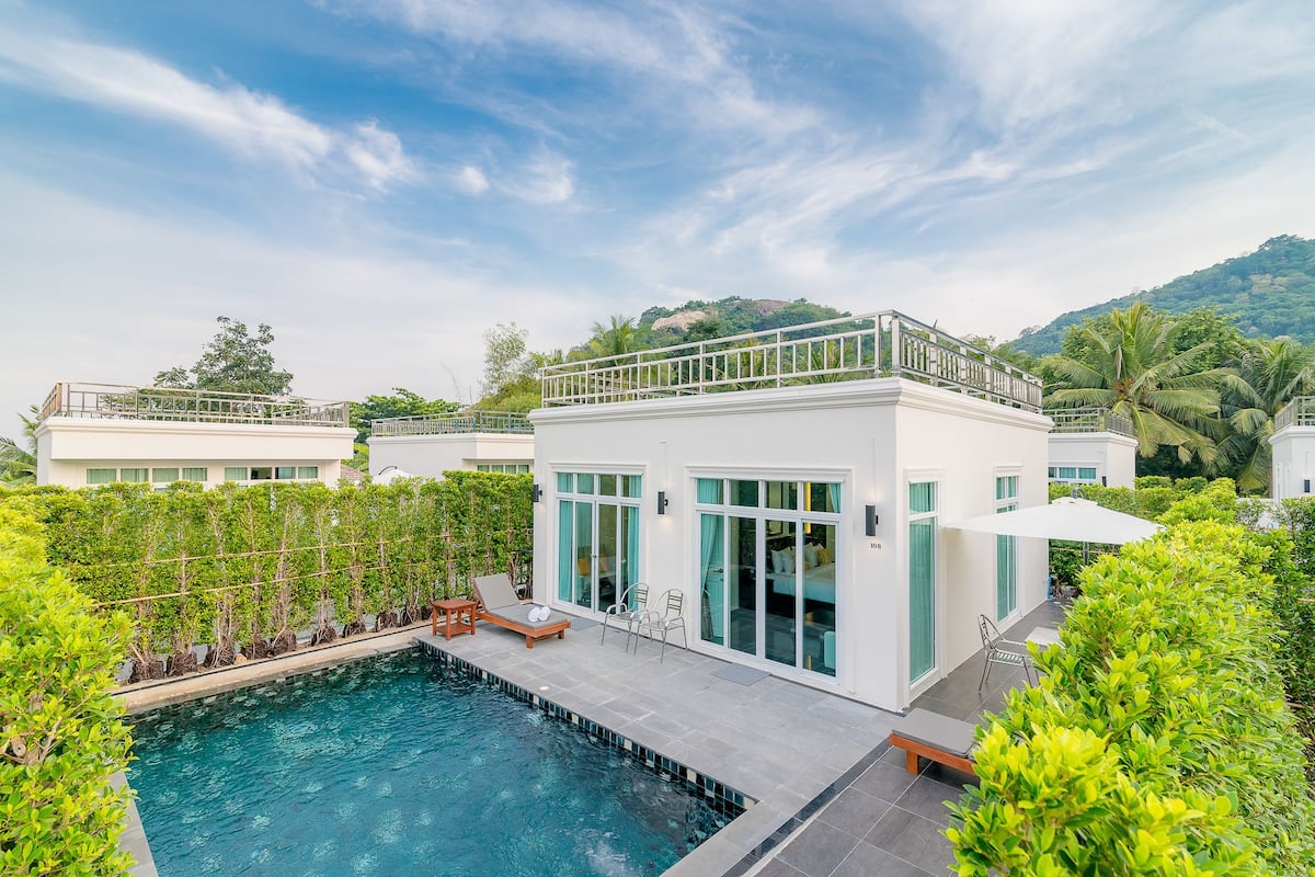 Un hôtel moderne doté d’une piscine, de grandes fenêtres et d’un balcon offrant une vue sur une végétation luxuriante.