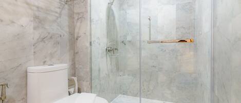 Ein modernes Badezimmer mit einer Duschkabine aus Glas, einer Toilette und einer Marmor-Spritzschutzwand.