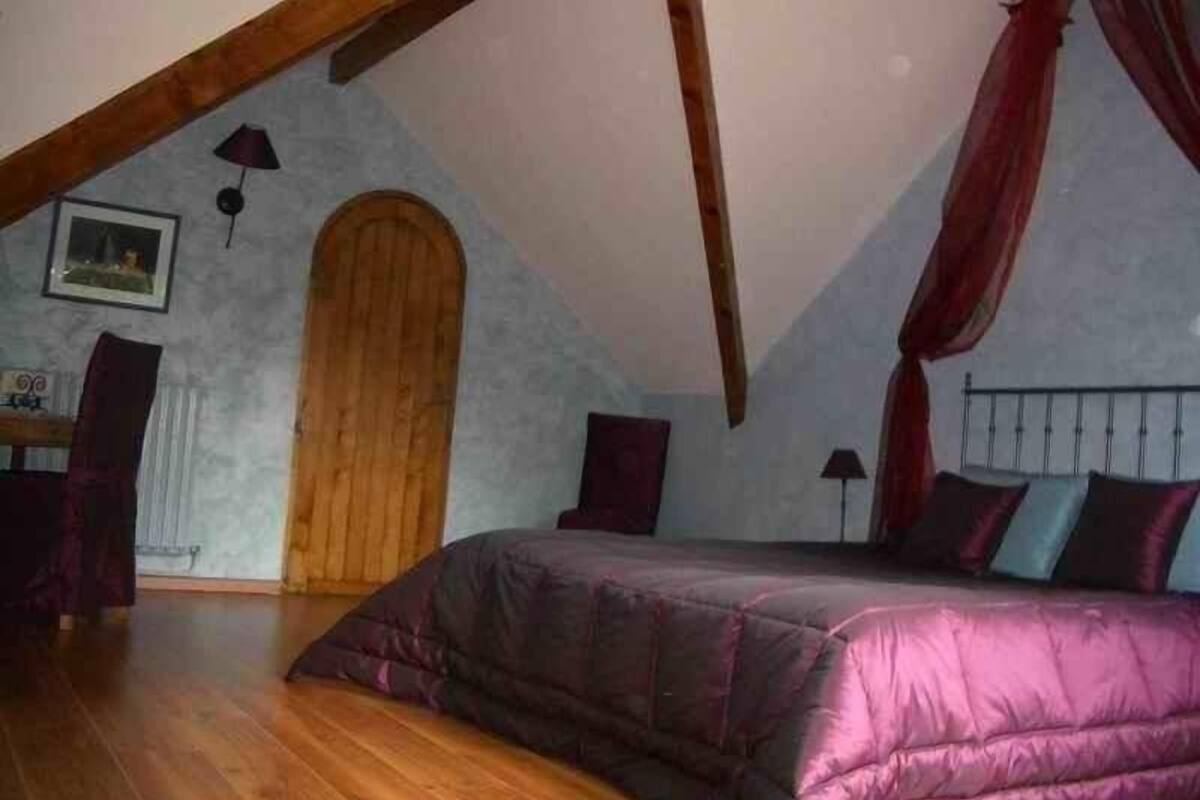 A bedroom with a sloped ceiling, a wooden door, a bed with a canopy, and a picture on the wall.