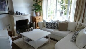 Una sala de estar moderna con chimenea, sofás blancos, una mesa de centro y una planta en maceta.