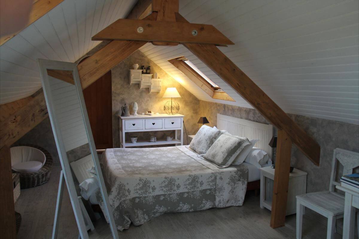 A bedroom with a sloped ceiling, a bed with a floral bedspread, a nightstand, a lamp, and a small white dresser.