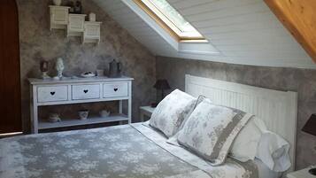 A bedroom with a sloped ceiling, a bed with patterned bedding, a nightstand with a lamp, and a dresser with decorative items.