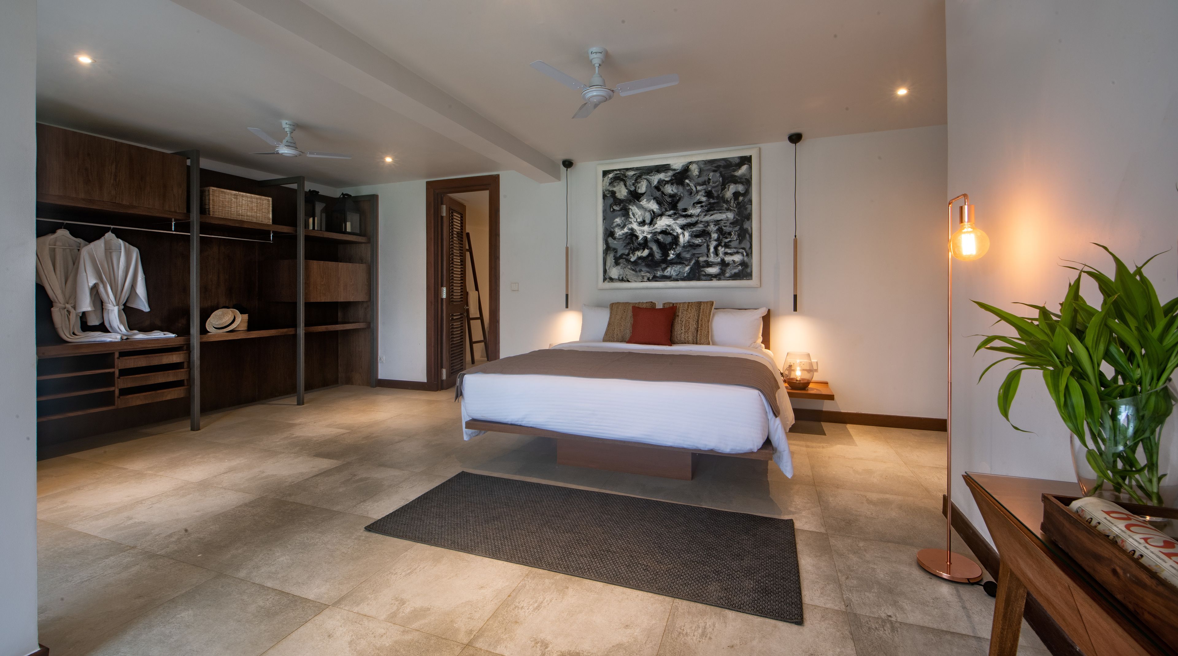 A modern bedroom with a large bed, a wardrobe, a ceiling fan, a floor lamp, and a potted plant.