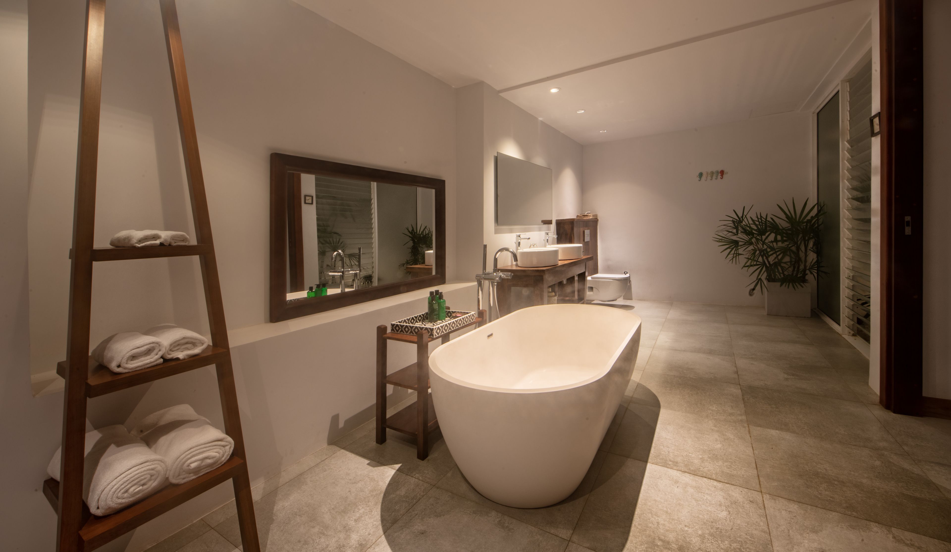 A modern bathroom with a freestanding bathtub, a wooden towel rack, a mirror, and a sink with a countertop.
