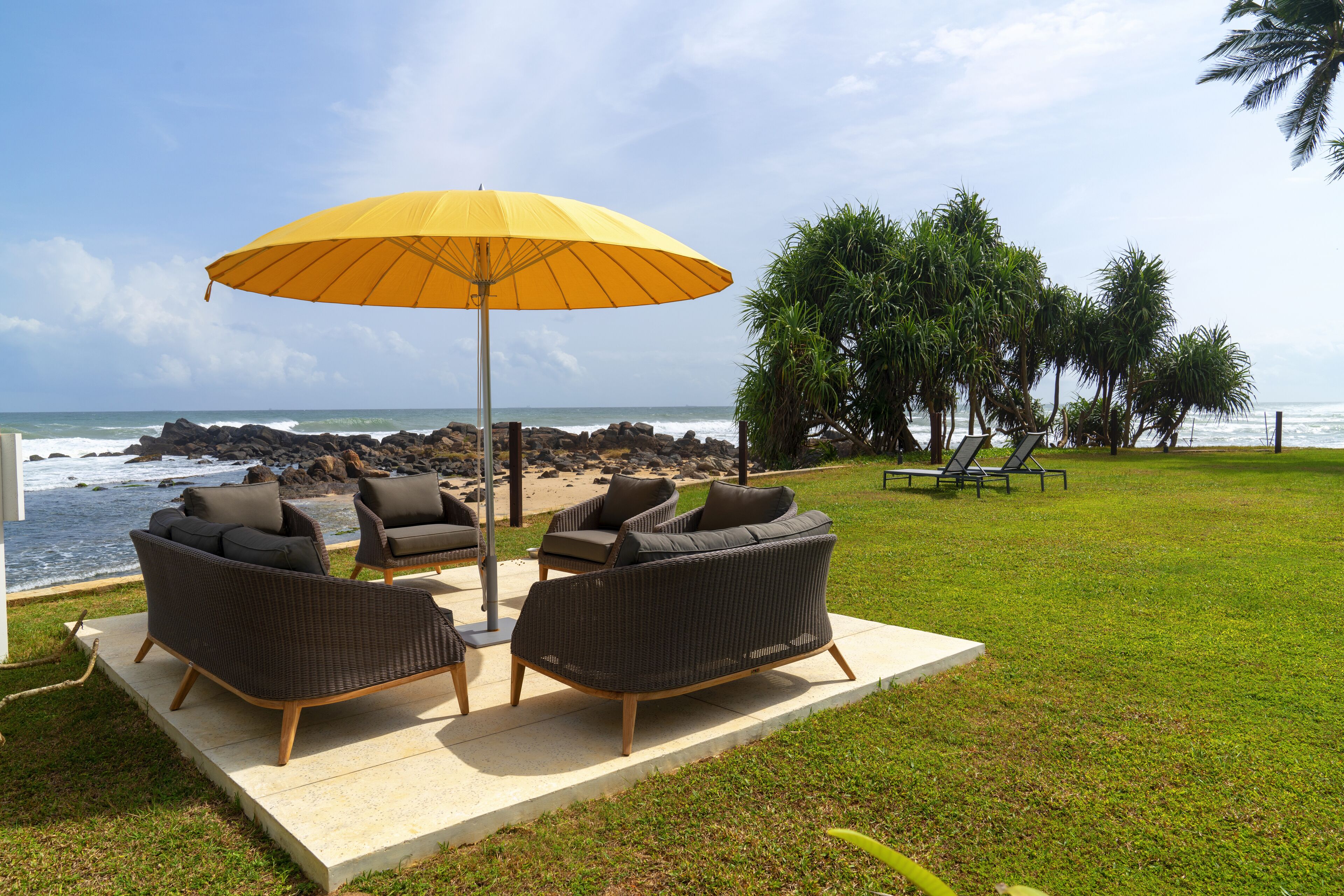 Eine Terrasse mit Korbmöbeln und einem gelben Sonnenschirm mit Blick auf das Meer.