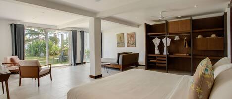 A spacious bedroom with a large bed, a seating area with a sofa and chairs, a walk-in closet, and a view of the outdoors through large windows.