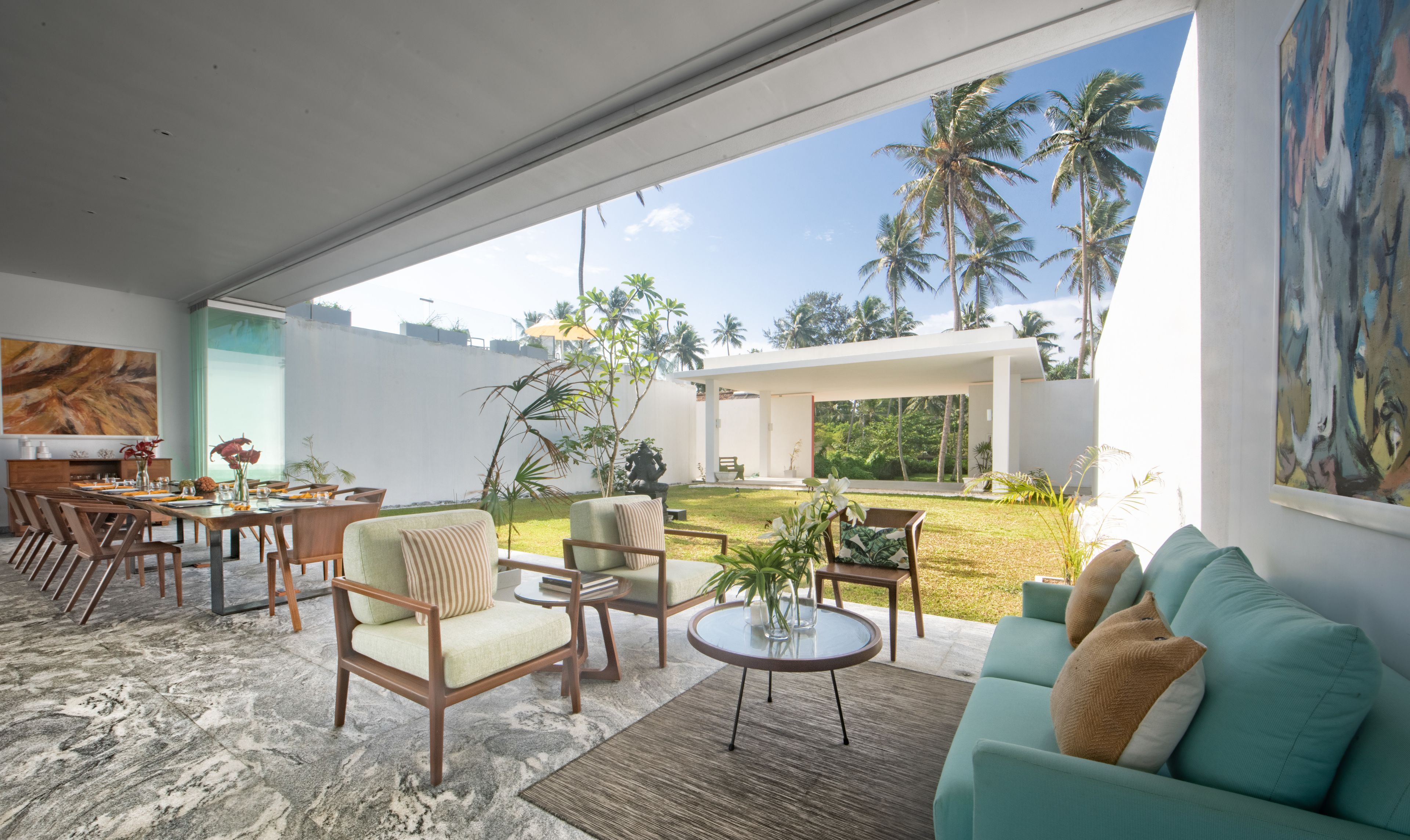 Una sala de estar moderna con un amplio ventanal que da a un espacio exterior privado, amoblada con un sofá, sillones y una mesa de comedor.