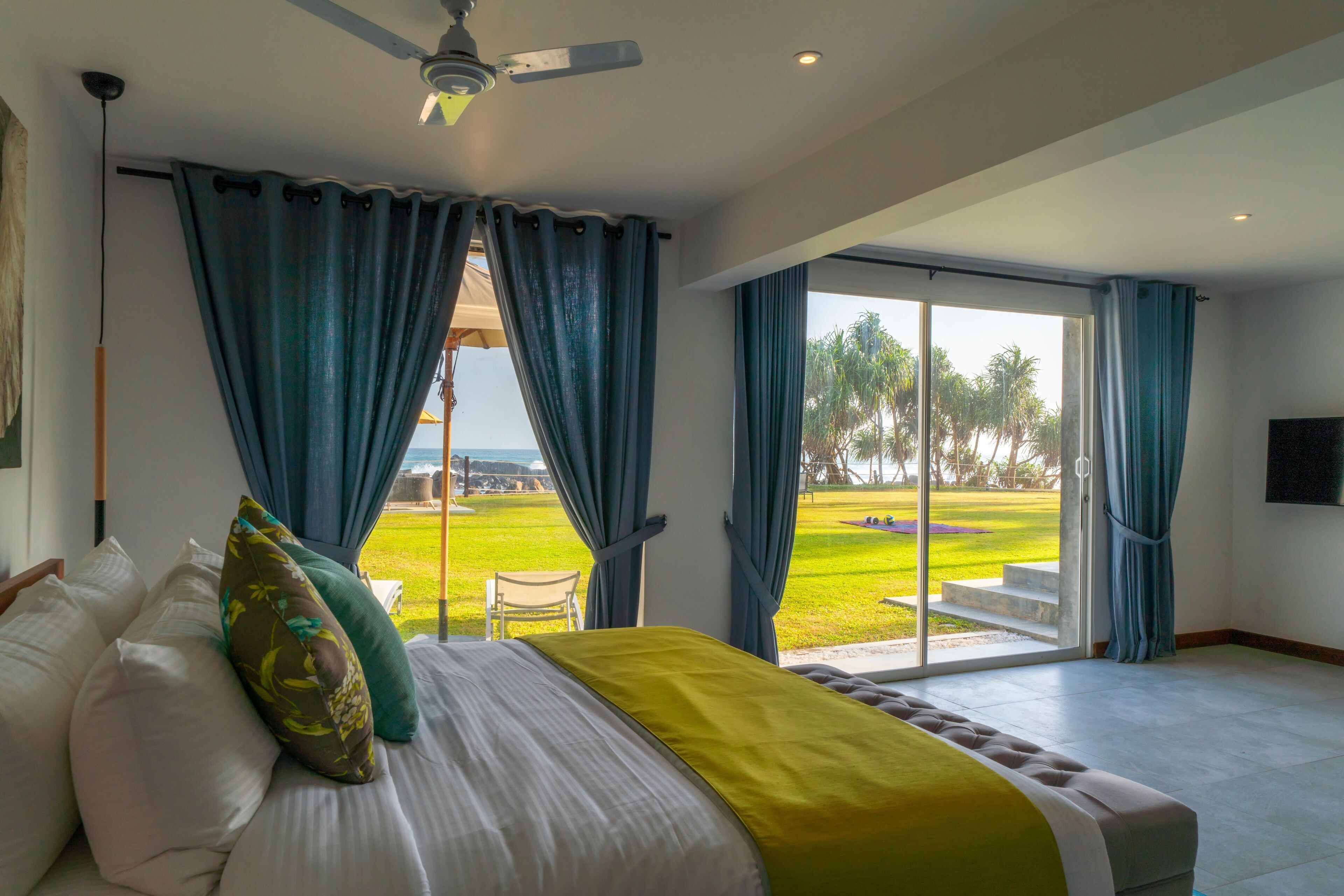 A bedroom with a bed, a ceiling fan, and a view of a grassy area through a glass door.