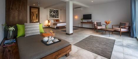 A modern hotel room with a large bed, a desk, two chairs, a TV, and a painting on the wall.