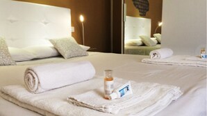 Una cama bien hecha con toallas blancas enrolladas, una botella de loción y un tubo de crema.