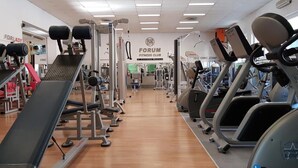 Un gimnasio con diversos equipos de ejercicio, incluyendo cintas de correr y máquinas de pesas, y un cartel que dice "FORUM FITNESS CLUB".