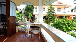 Un balcon avec une table et des chaises, entouré de verdure et offrant une vue sur un quartier résidentiel.