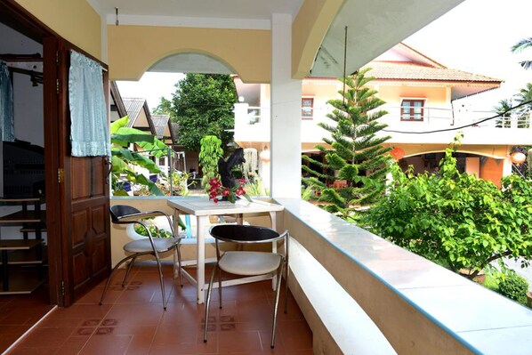 A balcony with a table and chairs, surrounded by greenery and a view of a residential area.