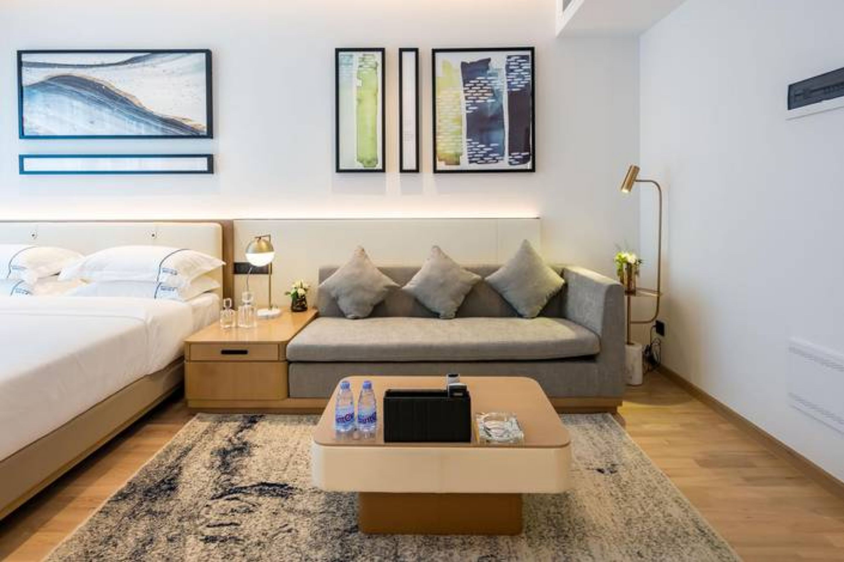A modern hotel room with a bed, a sofa, a coffee table, and artwork on the wall.