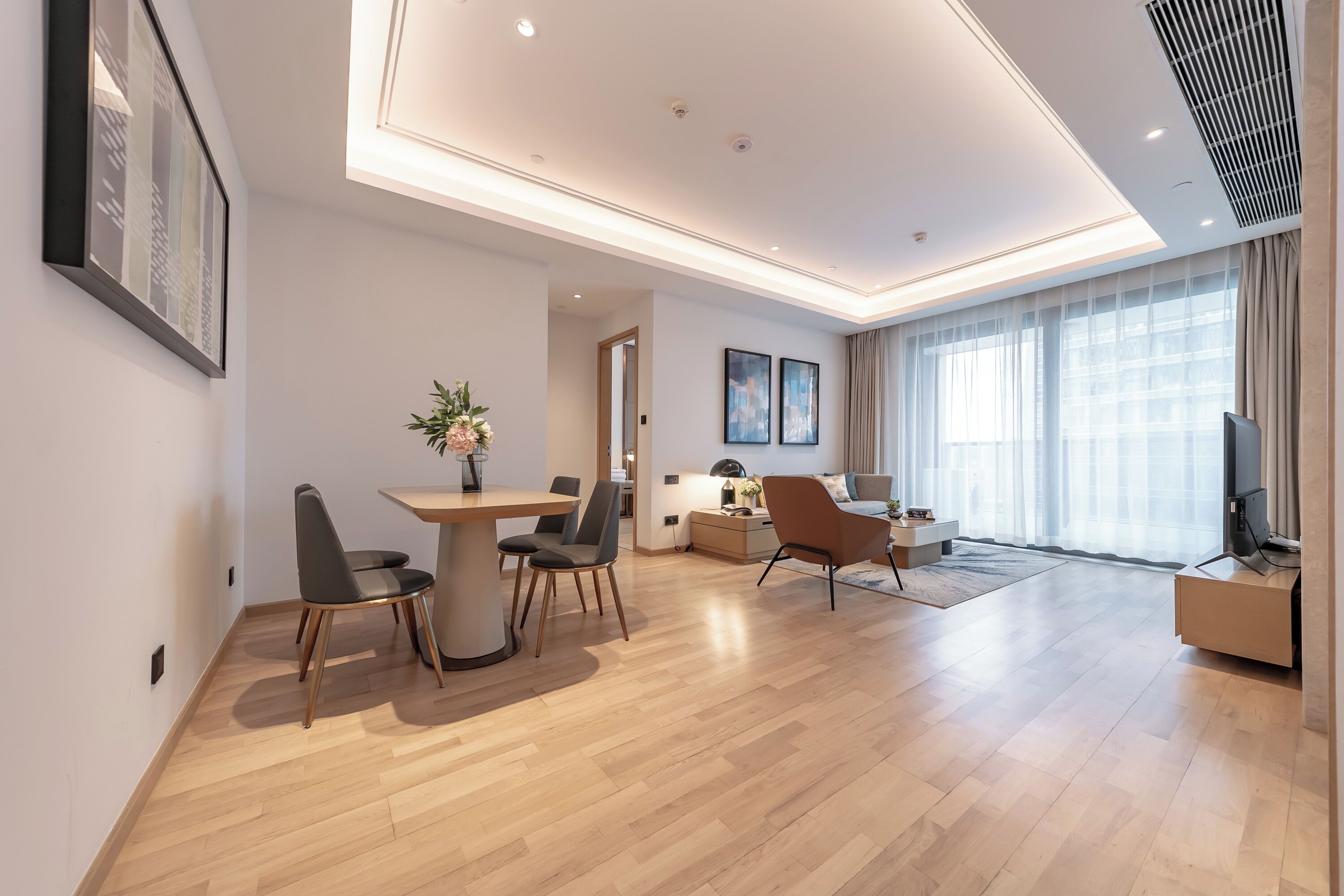 Una sala de estar moderna con comedor, televisor y un amplio ventanal con cortinas.