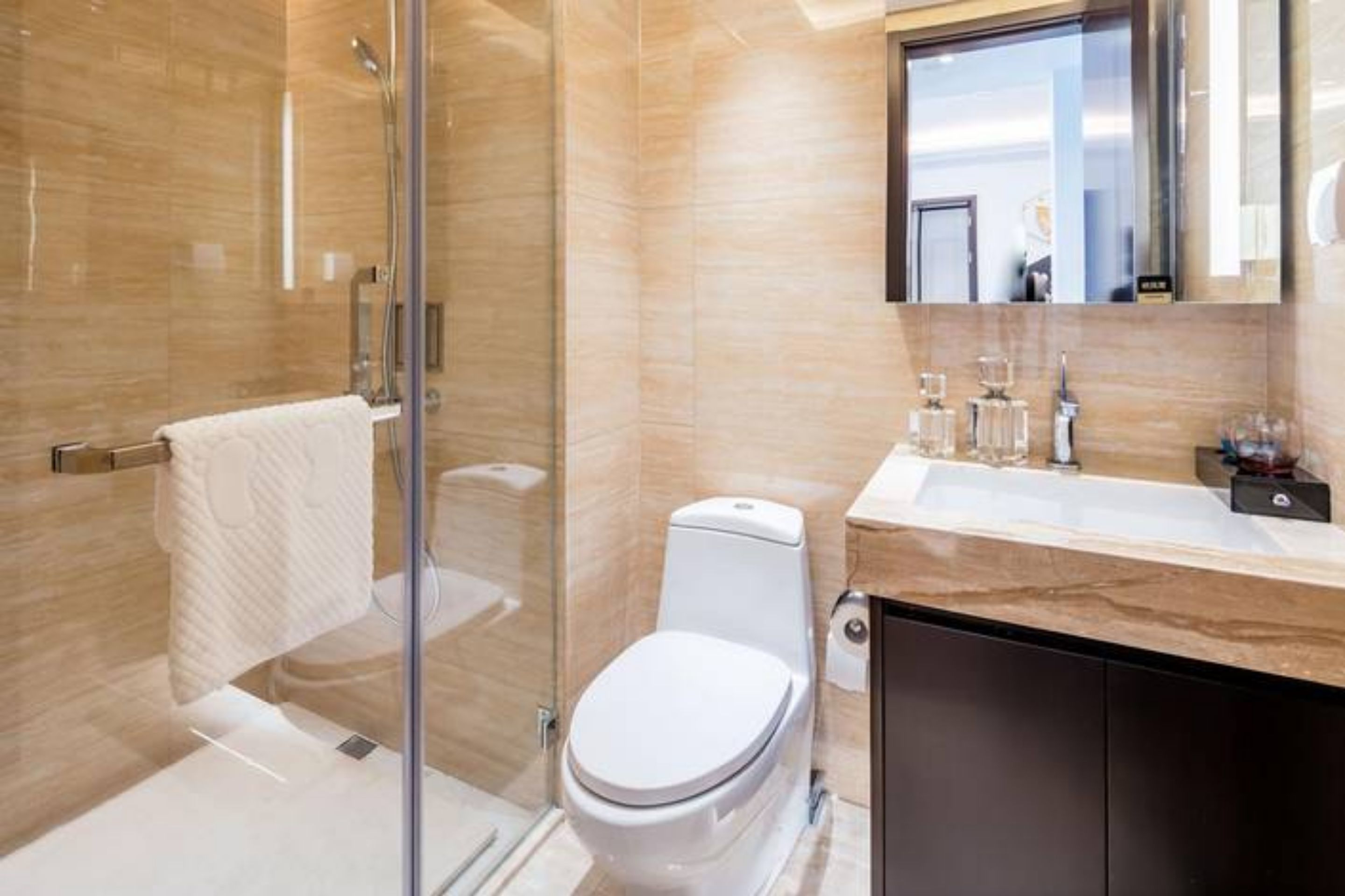 A modern bathroom with a glass shower enclosure, a white toilet, and a marble vanity with a sink and mirror.