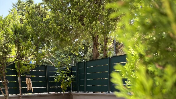 Un patio amueblado con mobiliario exterior, césped artificial y una valla verde.