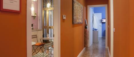 A hallway with orange walls, a tiled floor, and a door leading to a dining area with a table and chairs.