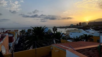 Un paisaje urbano costero al atardecer con edificios, palmeras y vistas al mar.
