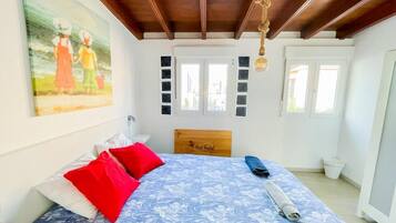 A bedroom with a wooden headboard, a bed with a floral bedspread, red pillows, and a painting on the wall.