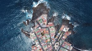 Vista aérea de un pueblo costero con un denso grupo de edificios, una calle estrecha y acantilados rocosos.
