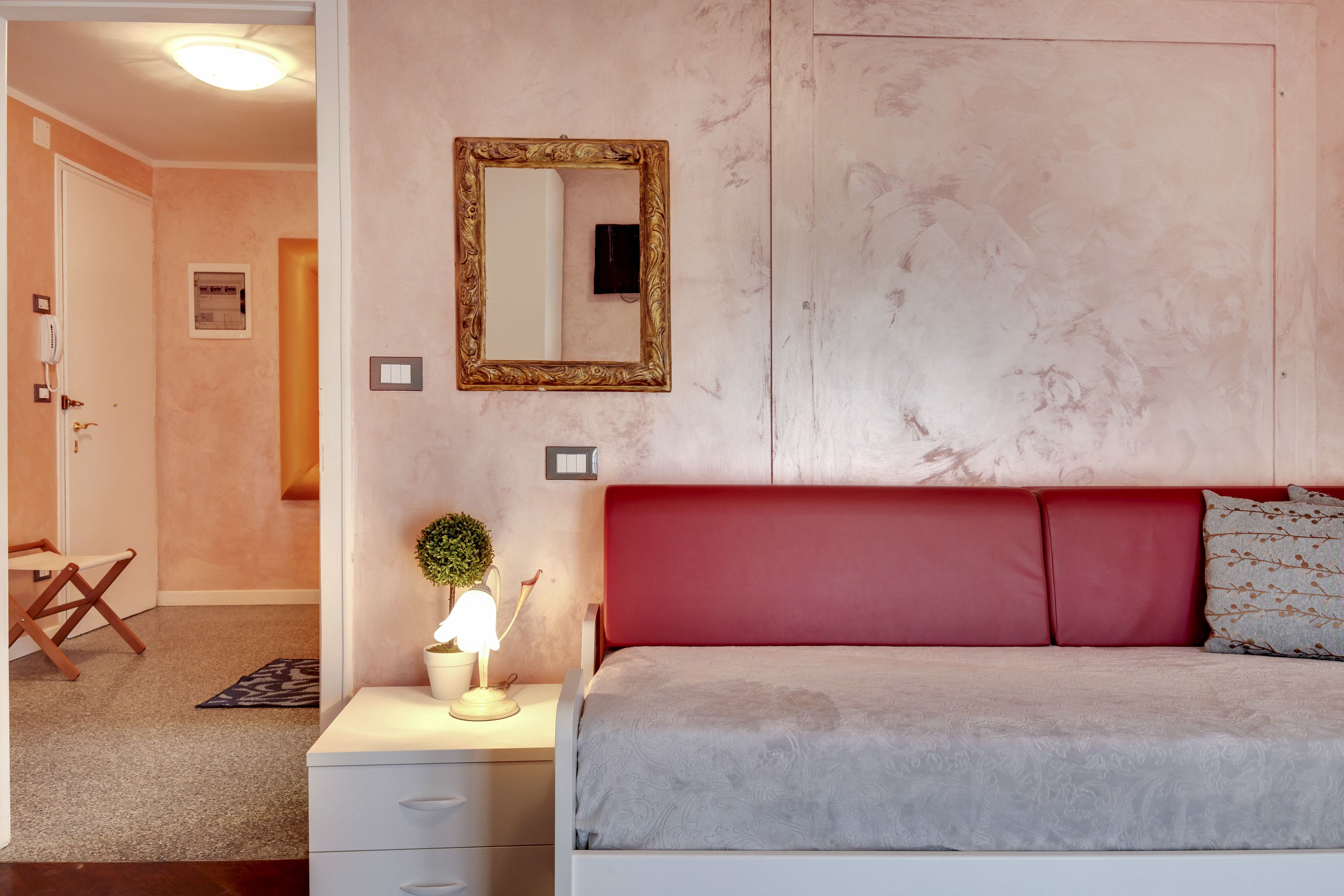 A bedroom with a red headboard, a bedside table with a lamp, and a mirror on the wall.