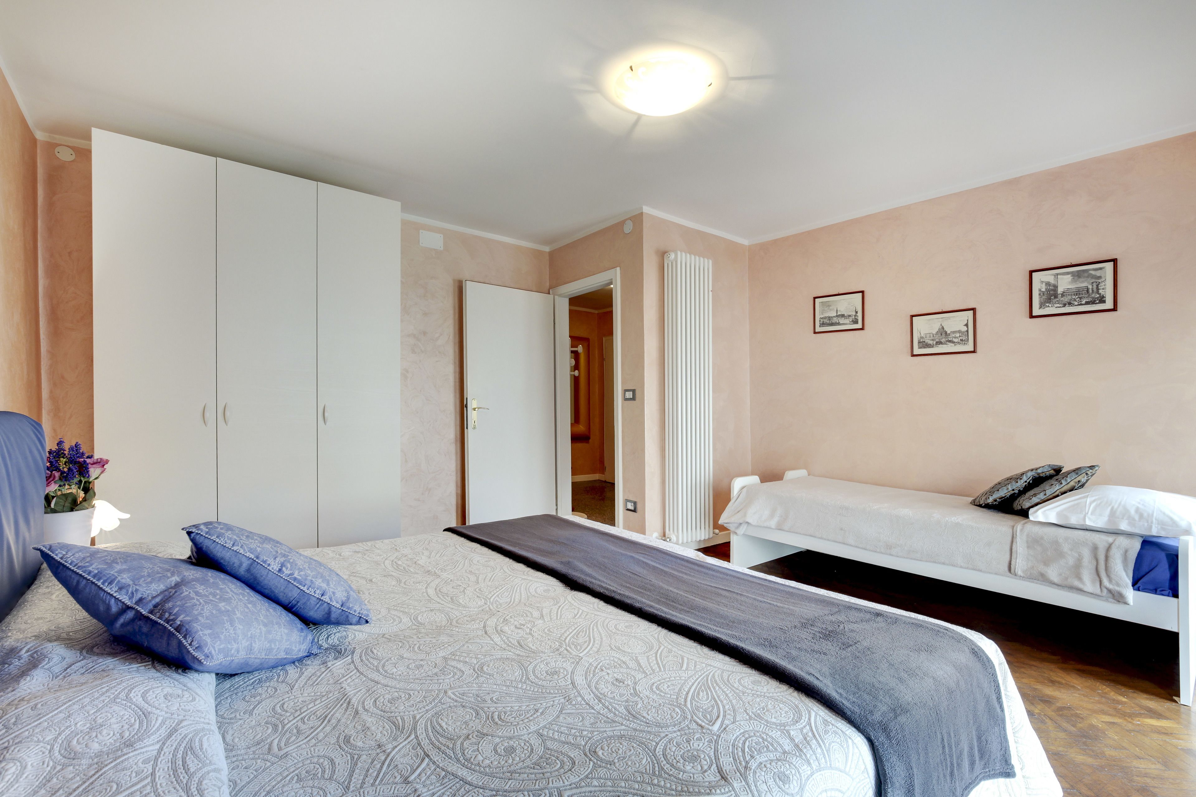 Une chambre avec un grand lit, un plus petit lit et une armoire. Des tableaux encadrés ornent le mur.