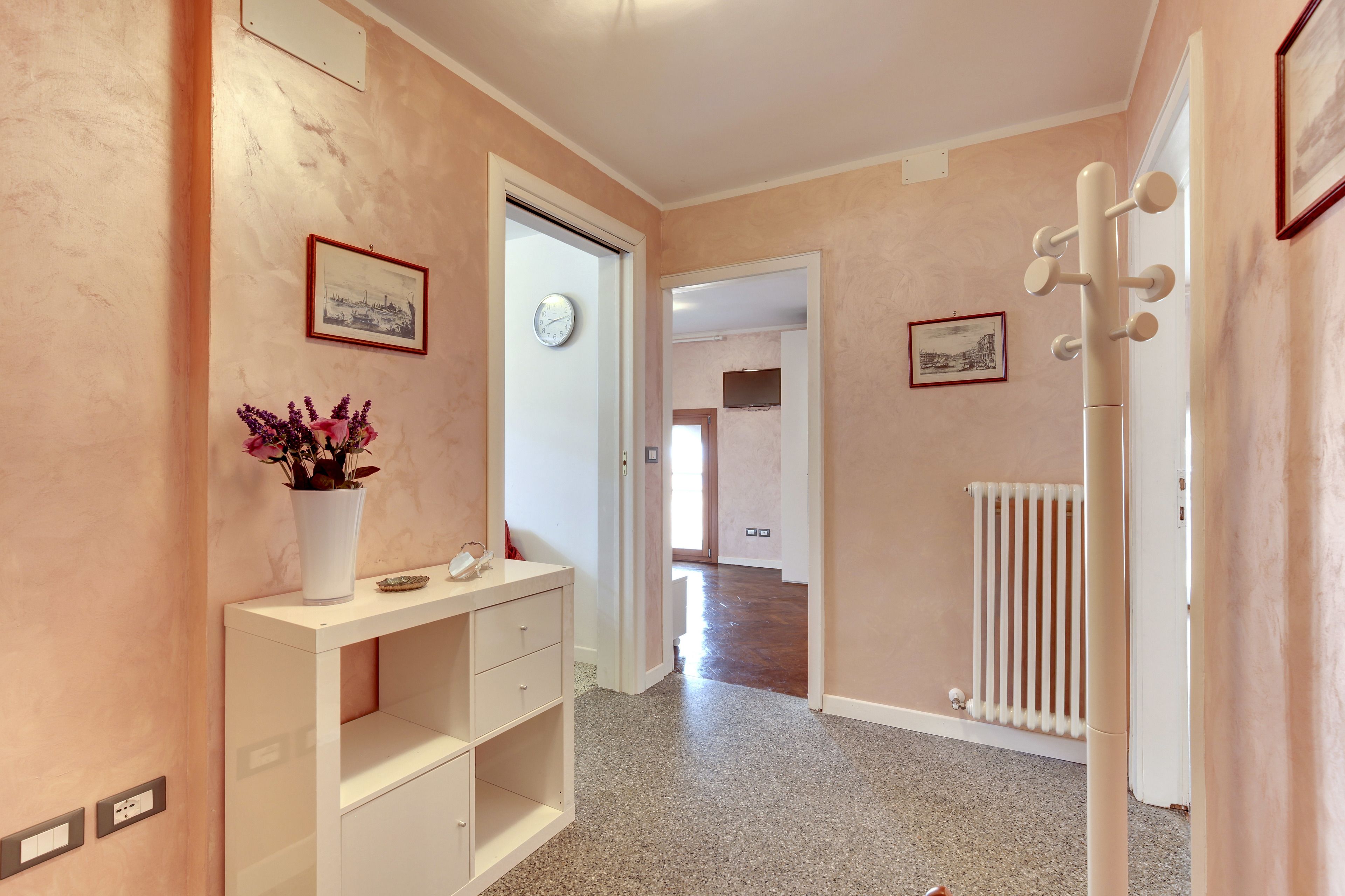 A hallway with a white console table, a clock, framed pictures, and a radiator.
