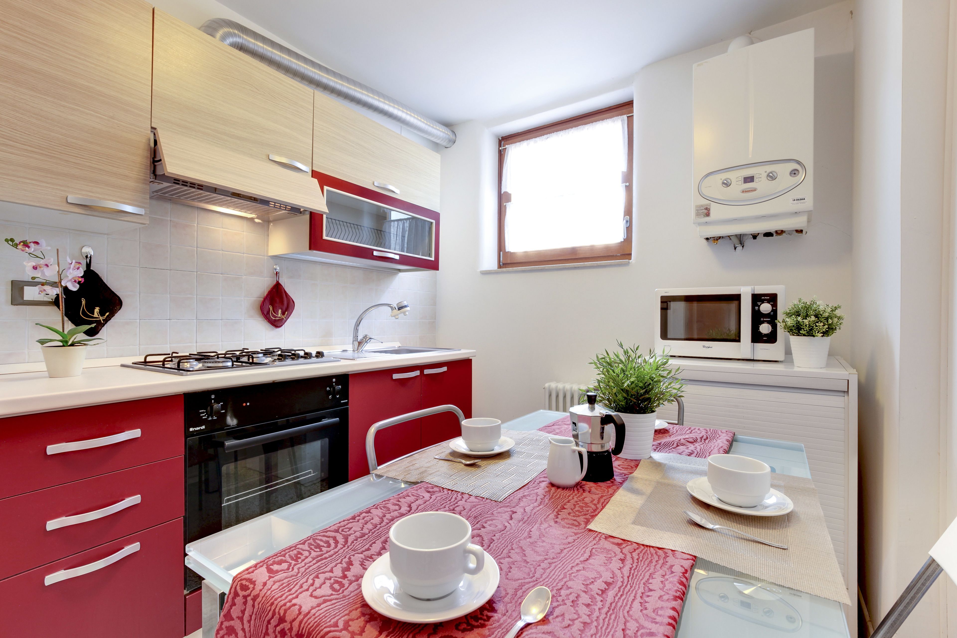 A compact kitchen with red and white cabinetry, a gas stove, a microwave, and a window providing natural light.
