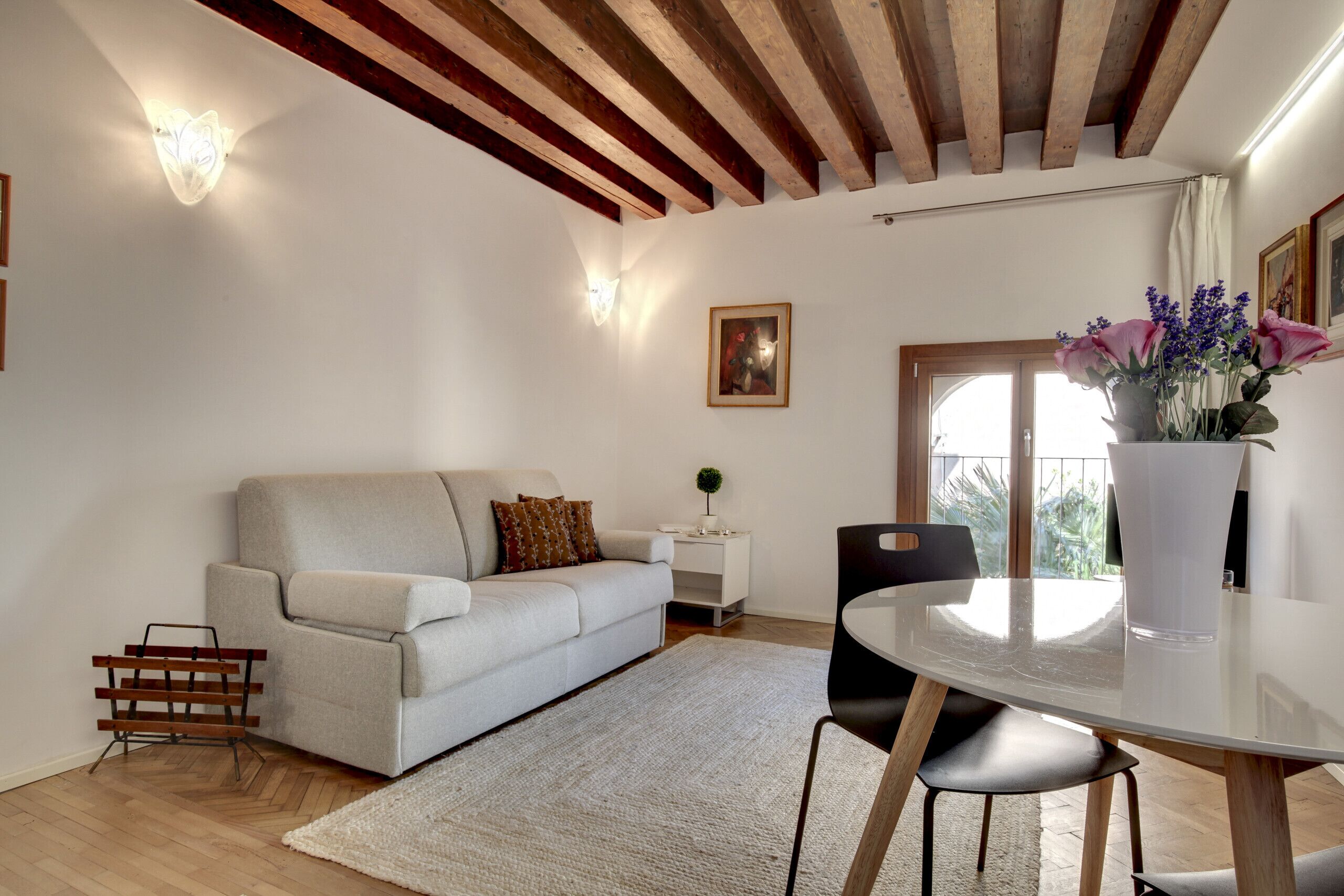 A modern living room with a sofa, a dining table, and a vase of flowers.