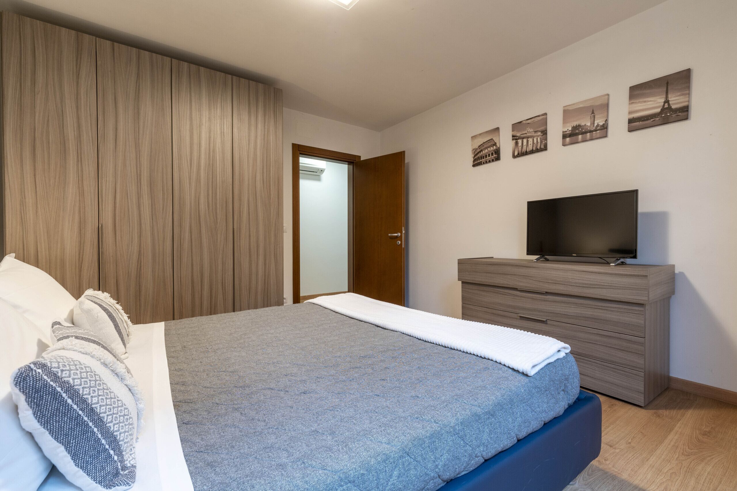 A bedroom with a bed, a dresser, a television, and a door leading to another room.