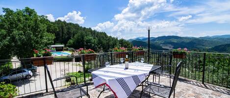 A terrace with a table set for dining, overlooking a pool and lush greenery.