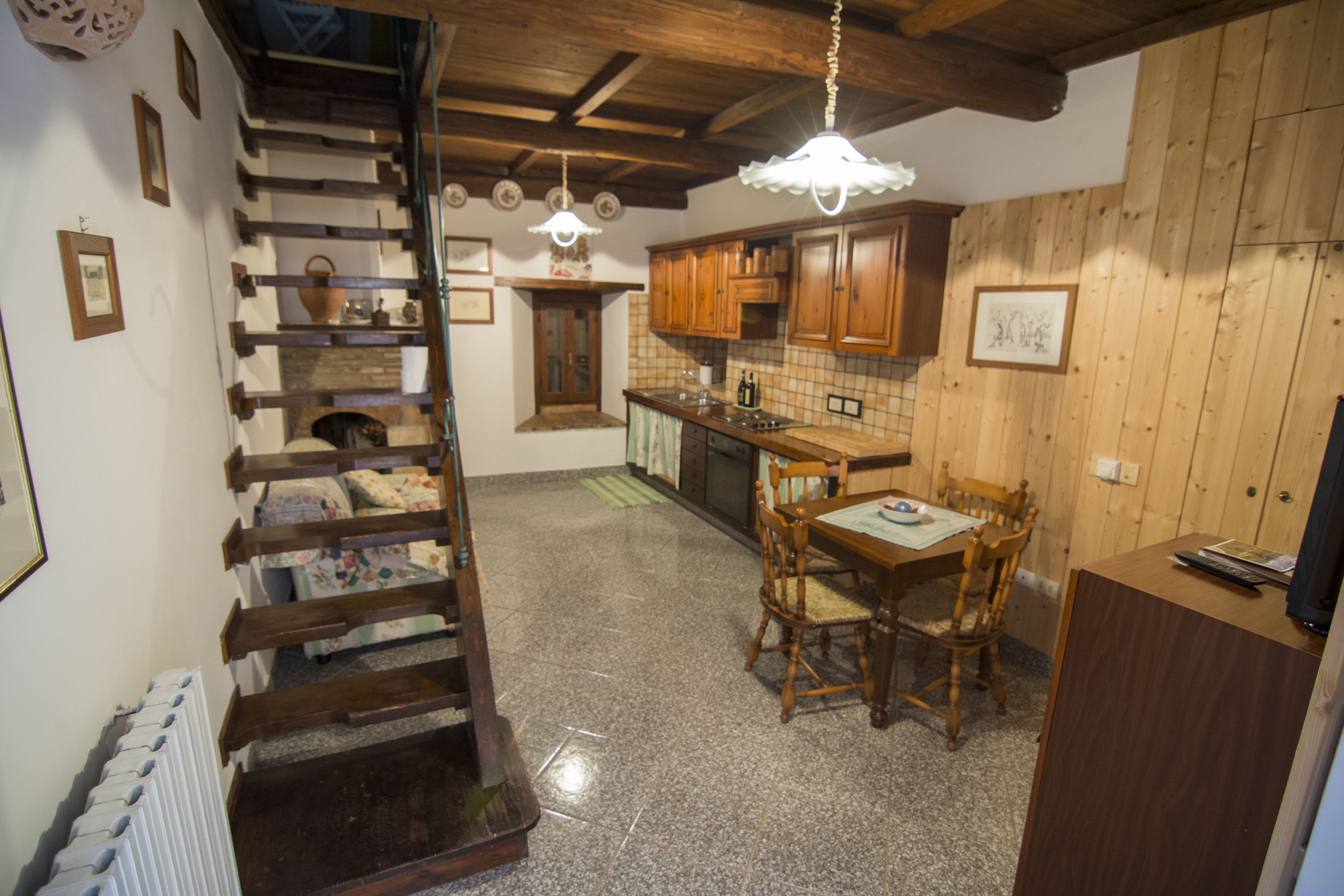 A rustic kitchen with wooden cabinets, a dining table with chairs, and a staircase with a wooden railing.