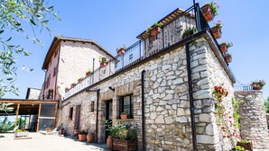 A stone building with balconies, potted plants, and a covered outdoor seating area. - Il Castello di Perchia (Spoleto)
