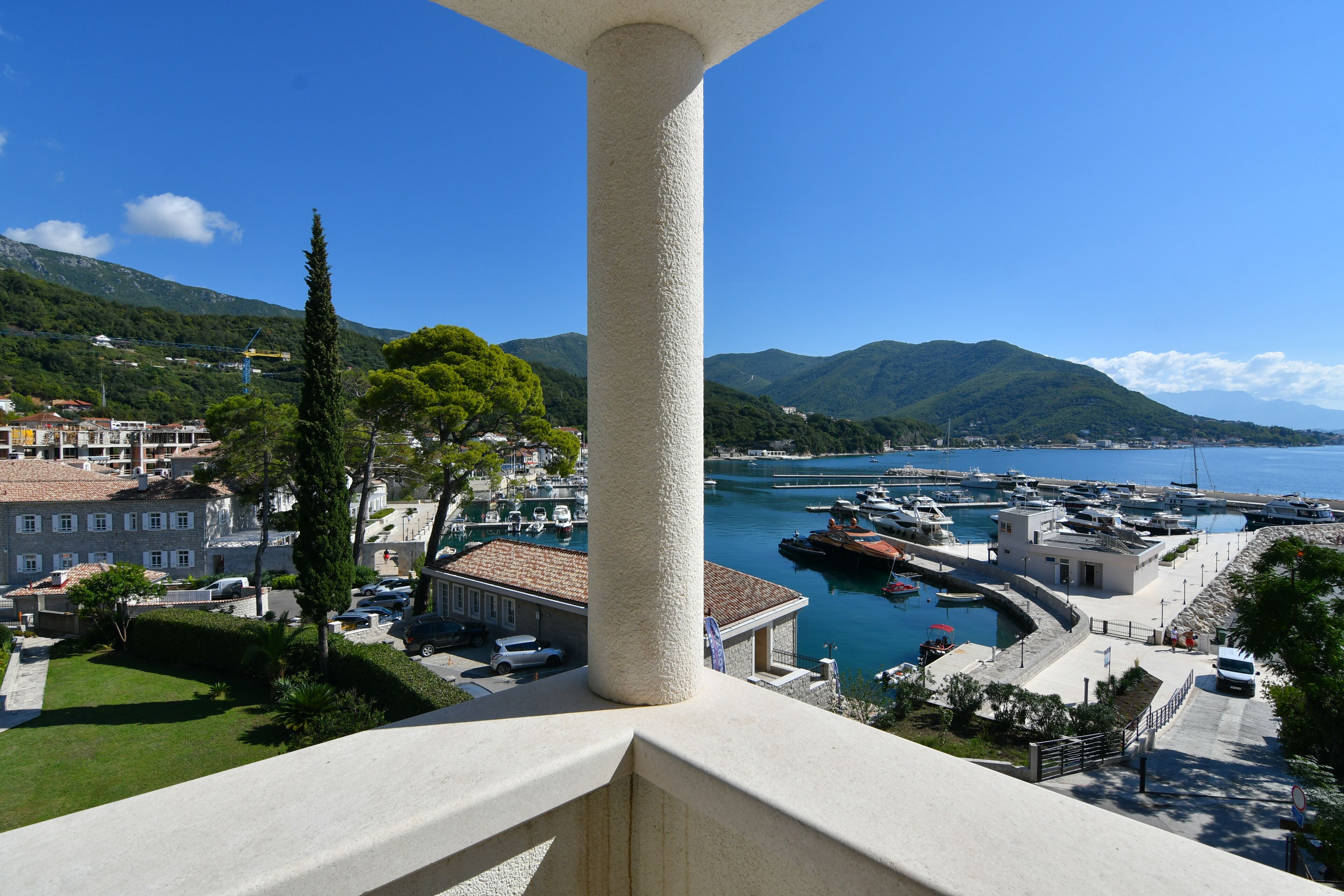 A coastal town with a marina, buildings, and mountains in the background.